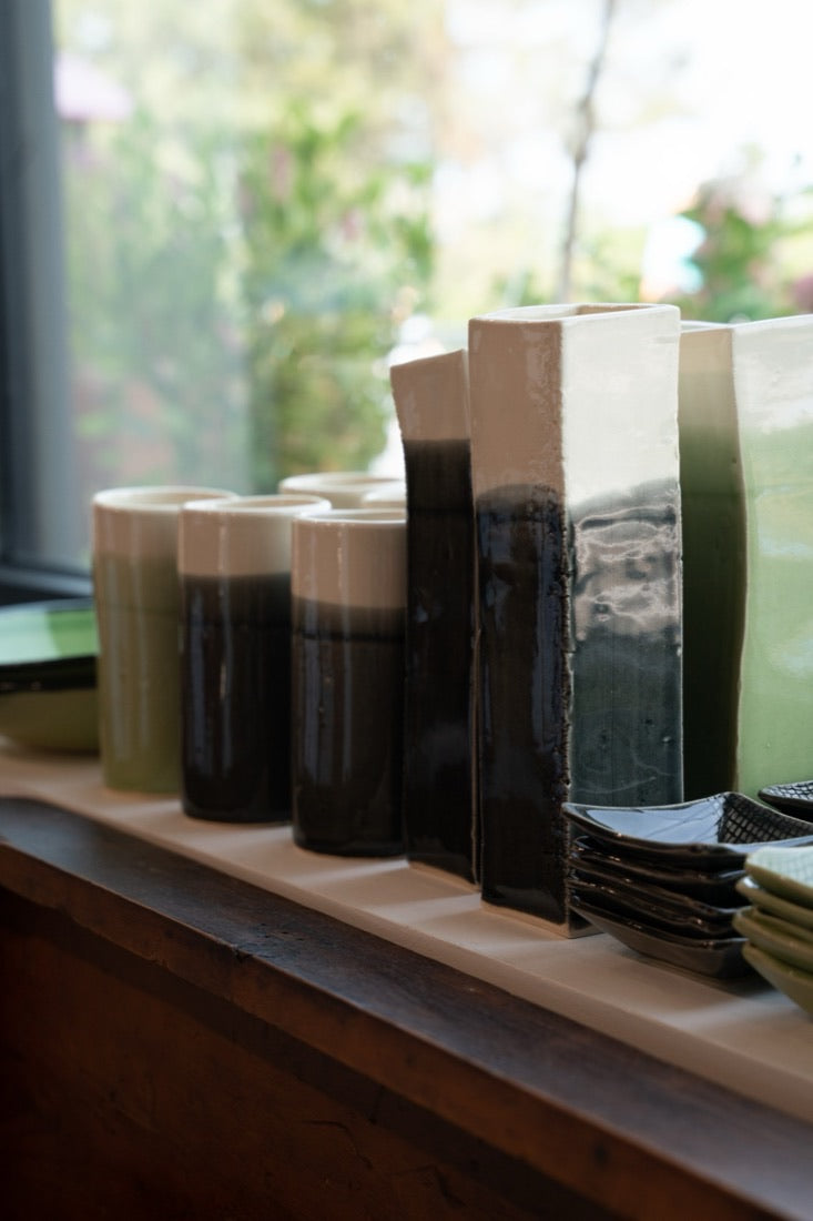 Tall black, white and green glazed ceramic vases lined up on a sunlit windowsill at the Cabin